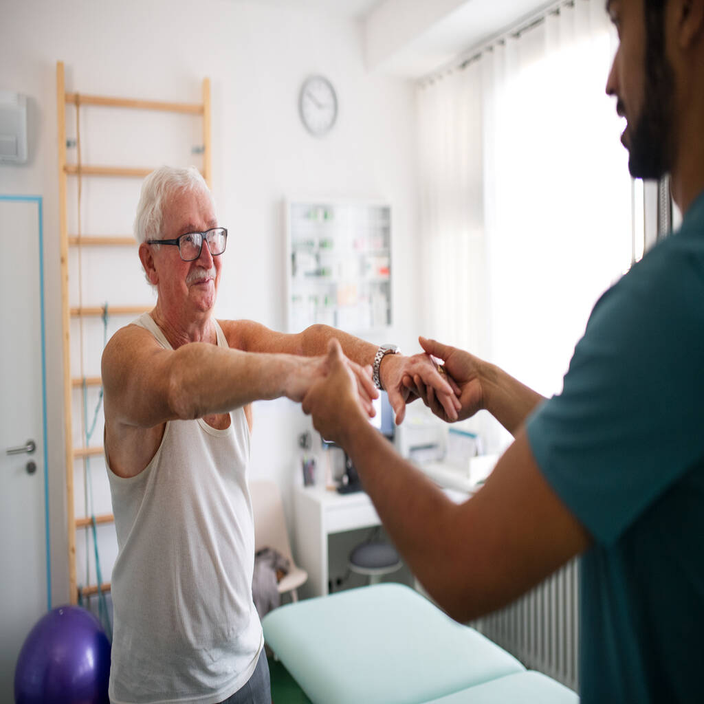 A young physiotherapist exercising with senior patient in a physic room.